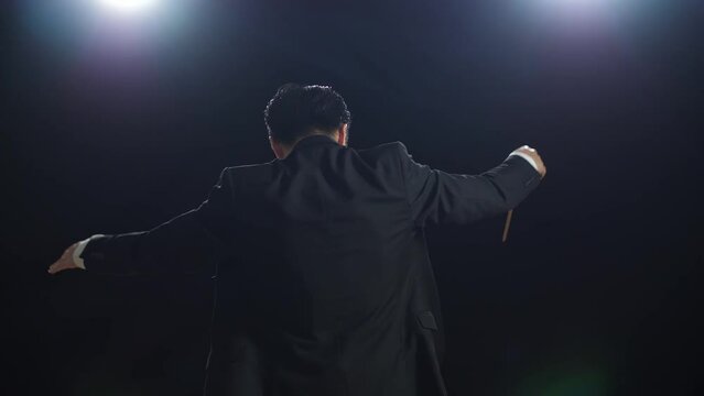 Back View Of Asian Conductor Man Holding A Baton And Showing Gesture In The Black Studio

