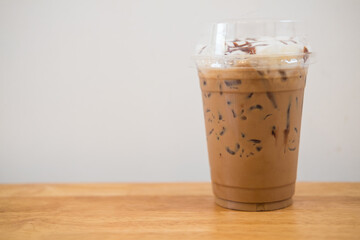Iced coffee in plastic cup on wooden table at cafe