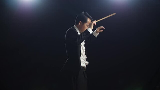 Side View Of Asian Conductor Man Holding A Baton Closing His Eyes And Showing Gesture Quickly In The Black Studio
