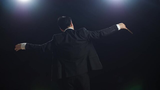 Back View Of Asian Conductor Man Holding A Baton And Showing Gesture In The Black Studio
