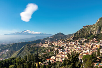 Fototapeta na wymiar Panoramic view on snow capped Mount Etna volcano on a sunny day seen from ancient Greek theater of Taormina, island Sicily, Italy, Europe, EU. Overview of hilltop village Taurmina. Travel destination
