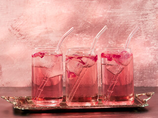 Three glasses of pink gin and rose lemonade on a light pink background
