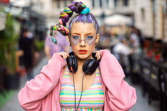 Cool funky young woman with trendy eyeglasses listening music on headphones outdoor