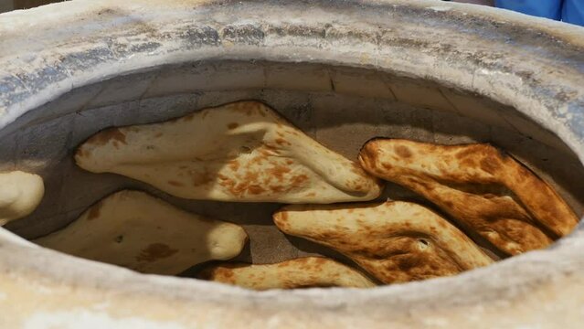 a baker bakes Georgian ojakhuri cakes in a tandoor, gluing raw dough to the wall of a hot stone tonir. National traditional bread. Slow motion, close up
