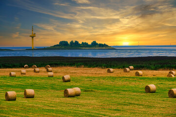 View over a meadow with straw bales to the Langlutjen peninsula near Bremerhaven/Germany at sunset