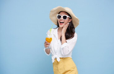 Beautiful smiling Asian woman in summer outfit with a glass of orange juice isolated on colorful blue background.