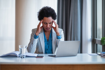 Stressed businesswoman having headache while using laptop at desk in office