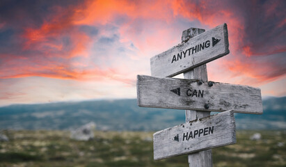 anything can happen text quote caption on wooden signpost outdoors in nature with dramatic sunset...