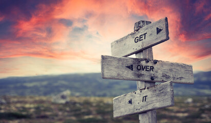 get over it text quote caption on wooden signpost outdoors in nature with dramatic sunset skies....