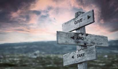 give and take text quote caption on wooden signpost outdoors in nature with dramatic sunset skies. Panorama crop.