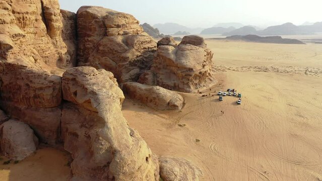 Aerial Panning Shot Of Off Road Vehicles By Rock Formations In Desert - Wadi Rum, Jordan