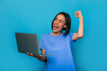 Close up portrait of shouting and an excited beautiful modern woman while she holds laptop and...
