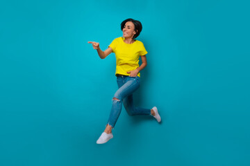 Full-length photo of excited attractive shouting modern woman in yellow t-shirt while she jumping, pointing and moving forward