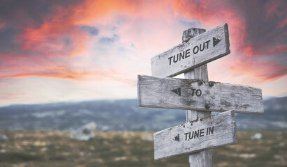 tune out to tune in text quote caption on wooden signpost outdoors in nature with dramatic sunset skies. Panorama crop.