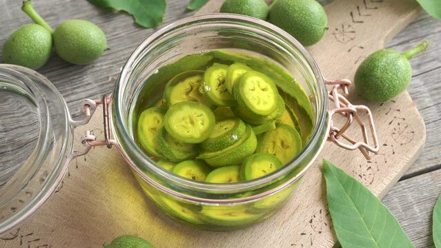 Pouring cut up unripe walnuts into alcohol in a jar, to prepare homemade nut liqueur