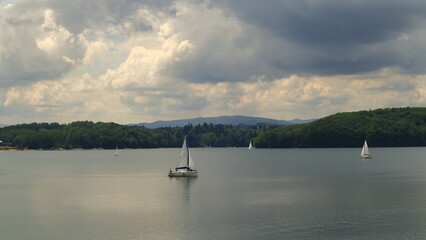 A white sailboat on the Soliński lake. Dark leaden clouds in the sky. Biała żaglówka na jeziorze Solińskim. Ciemne ołowiane chmury na niebie. © jarizPJ