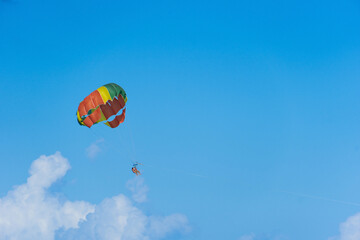 Parasailing is an extreme sport, people fly by parachute against the blue sky. Marine entertainment, bright parachute, blurry figures of people. Copy space.