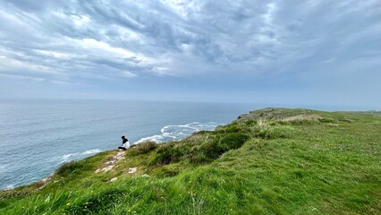 unrecognizable person sitting observing on a cloudy day the sea of Cabo de Ajo in Cantabria Spain