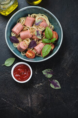 Green bowl with threaded spaghetti hot dog bites, flat lay on a dark-brown stone background, vertical shot with copyspace