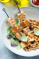 Skewers with roasted chicken meat and haloumi cheese served in a beige plate with roasted chickpeas, close-up, vertical shot