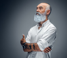 Studio shot of elegant pensive grandfather with tattooes dressed in white shirt.
