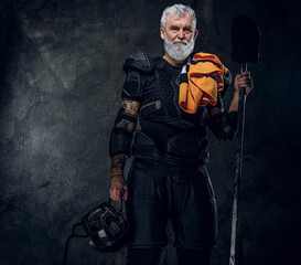 Fototapeta na wymiar Shot of tattooed elderly hockey player with headwear and hockey stick against dark background.