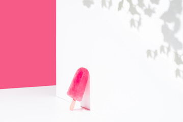 Paleta de hielo con sabor a frambuesa apoyada contra una pared blanca. Palo de helado rosa. Espacio para texto