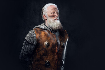 Portrait of aged knight with long beard dressed in antique armor against dark background.