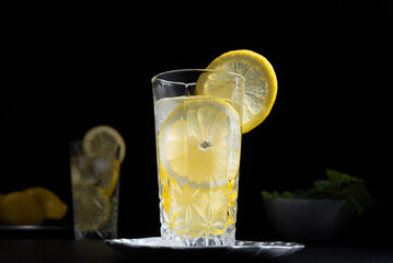 Dos vasos de refrescante zumo de limón, cóctel de frutas con rodajas de limón y hielo sobre fondo negro