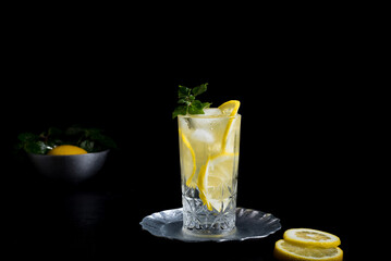 Un vaso de refrescante zumo de limón, cóctel de frutas con rodajas de limón y hielo sobre fondo negro