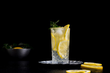 Un vaso de refrescante zumo de limón, cóctel de frutas con rodajas de limón y hielo sobre fondo negro