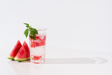 Un vaso de zumo de sandía con trozos de sandia y hielo sobre fondo claro	