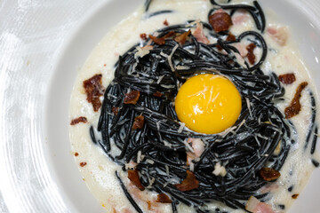 Carbonara black spaghetti topping with raw yolk which is severed in white dish, fusion food menu....