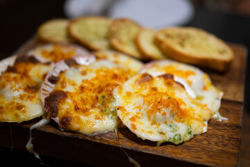 Baked cheesy scallops which are served on wooden plate. Seafood meal photo, Close-up and selective focus at front piece.