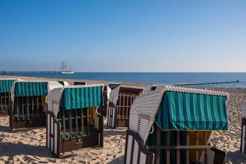 Papier Peint photo Heringsdorf, Allemagne Strandkorb and Pier in Bansin, Usedom. Hooded Wicker beach chairs on a beach with a barque in the background.