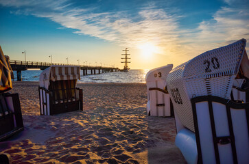 Strandkorb and Pier in Bansin, Usedom. Hooded Wicker beach chairs on a beach with a barque in the...
