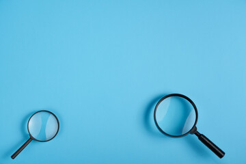 Two magnifying glass big and small lying on blue background, top view with negative space above