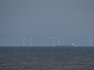 Ocean Wind Farm on Horizon with Ship Sailing Past Right to Left against blue sky