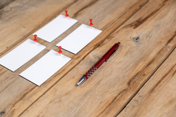 Blank business cards and a pen against a wooden background. Four white paper rectangles were pinned...