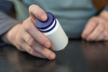 An adult man holds a white vial in his hands.