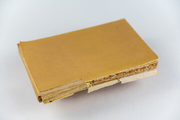 An old tattered book against a neutral background. Brown pages. Softcover. Torn text blocks. Selective focus.