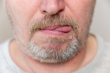 The lower part of a man's face. Mature man with stubble sticks out his tongue at the edge of his...