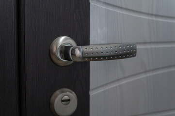 Doorknob. Chrome door handle on a white and brown front door. Close-up. Selective focus.