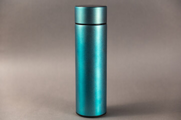 A modern thermos against a gray background. Cylindrical vacuole flask in turquoise color. Container for hot and cold drinks. Equipment for sports, hiking, and travel.