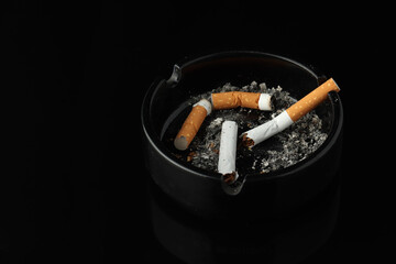 Burning cigarette left in ashtray on black background. Drugs are harmful to the lungs.