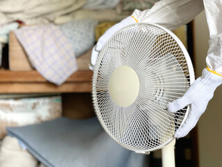 物のあふれた押し入れの前で扇風機を持つ軍手をはめた手元2