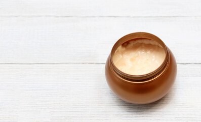 Body or face care cream in a round golden jar on a white wooden background with a place for text.
