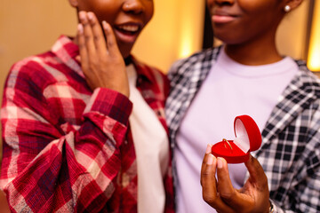 multicultural woman making proposal to her girlfriend in pajamas together in room at evening , Lgbt...