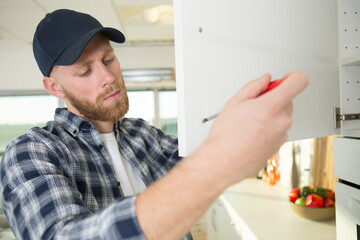 man using screwdriver to install a kitchen cupboard