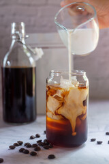 pouring milk in to a glass of homemade cold brew coffee on white table background.